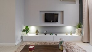 Ein modernes Wohnzimmer mit einem Wand-Fernseher, einer weißen Ablage, Dekorationselementen und einem Couchtisch.