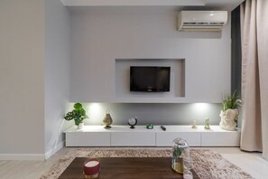 Ein modernes Wohnzimmer mit einem Wand-Fernseher, einer weißen Ablage, Dekorationselementen und einem Couchtisch.