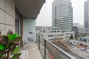 Ein Balkon mit einer Hängematte, Blick auf eine Stadtlandschaft mit modernen Gebäuden und einer Straße darunter.