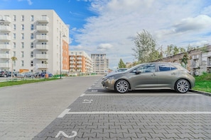 Ein Parkplatz mit einem Auto, Gebäuden im Hintergrund und blauem Himmel.