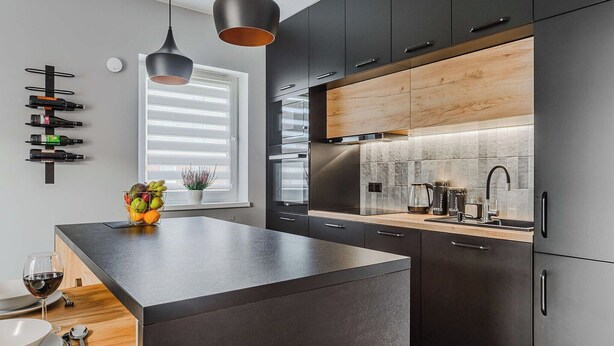 Een moderne keuken met donkere kastjes, een centraal eiland, hangende verlichting en een raam met zonwering.