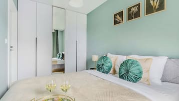 Un dormitorio con cama, almohadas, mesita de noche, lámpara y espejo.