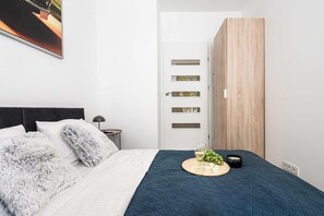 A modern bedroom with a bed, a nightstand, a lamp, a wardrobe, and a wall-mounted shelf. - Warsaw Flat with City Views (Warszawa 2)
