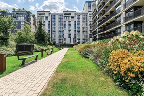 A pathway leading to a modern apartment building with multiple balconies and a well-maintained garden with flowers. - Warsaw Flat with City Views (Warszawa 2)