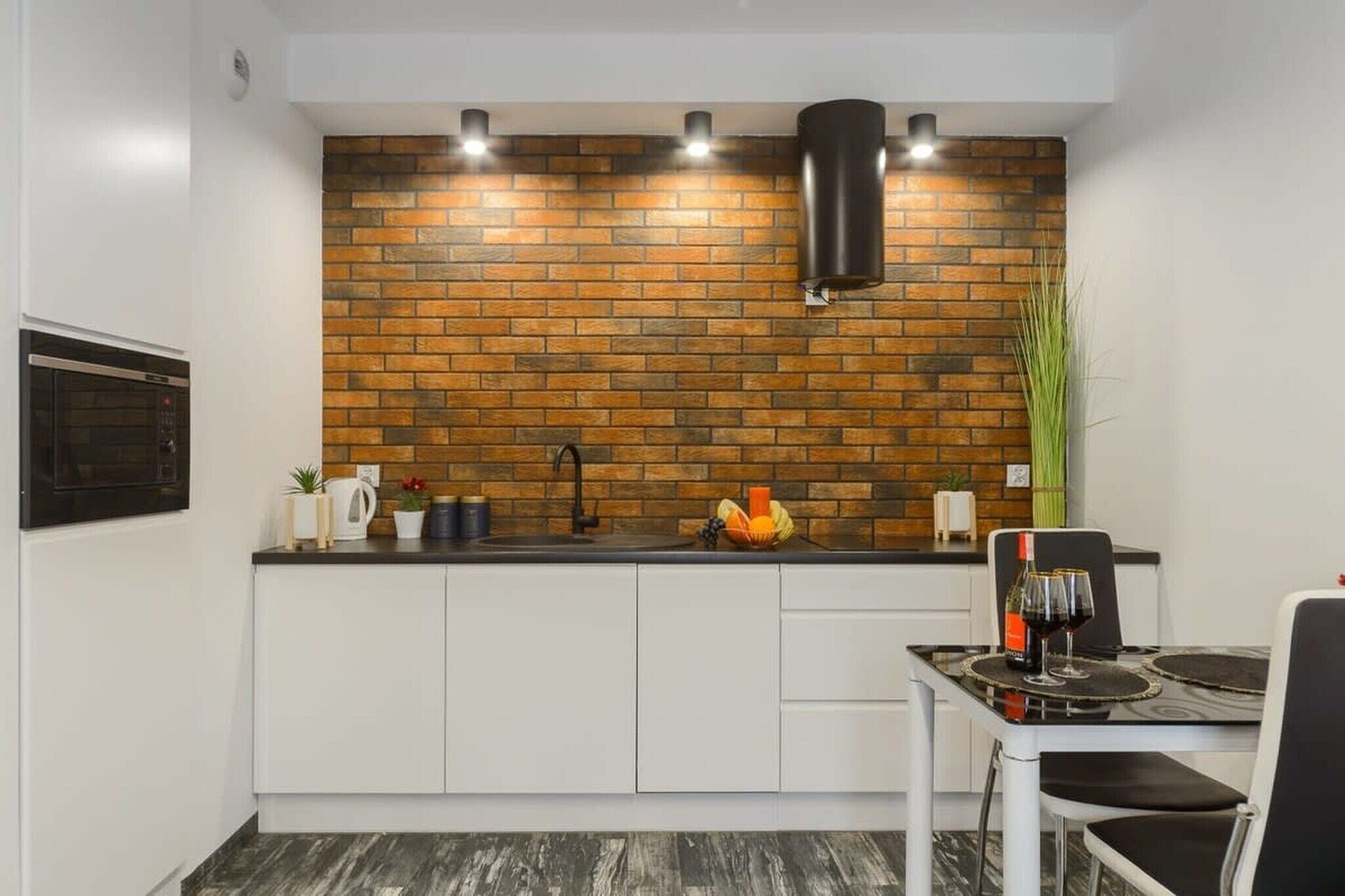 A compact kitchen with a brick backsplash, white cabinetry, and a dining area with a table and chairs.