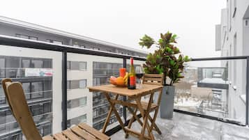 A balcony with a wooden table, a chair, a potted plant, a bottle of wine, and a glass of wine.