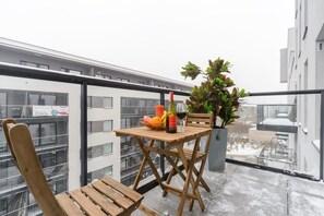 Ein Balkon mit Holztisch, einem Stuhl, einem Blumentopf, einer Weinflasche und einem Weinglas.