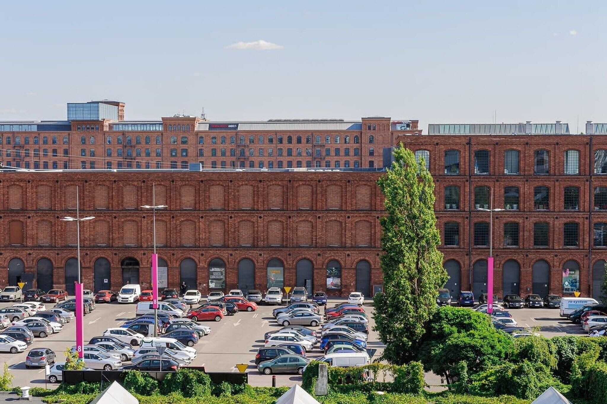 A parking lot with multiple cars and a large brick building in the background.