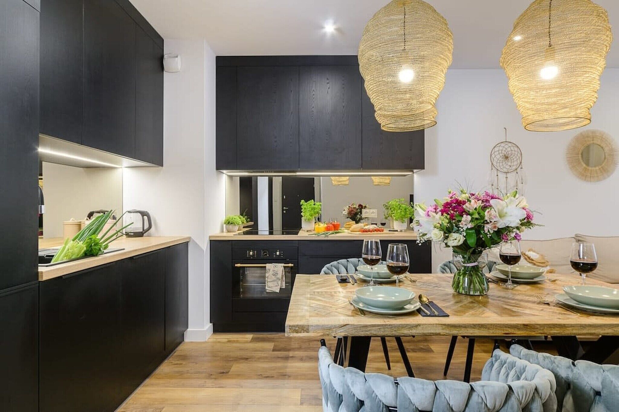 A modern kitchen with dark cabinetry, a wooden dining table set for two, and a hanging light fixture.