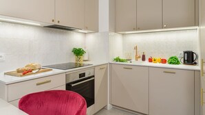 Eine moderne Küche mit weißen Schränken, einer Edelstahl-Dunstabzugshaube, einem Einbauofen und einem roten Stuhl.