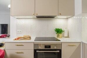 Ett modernt kök med en inbyggd ugn, en bänkskiva med en skärbräda och grönsaker, och en väggmonterad växt.