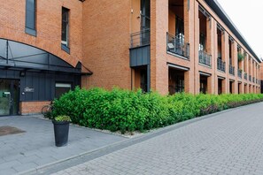 Ein modernes Gebäude mit Backsteinfassade, großen Fenstern und einer gepflegten Hecke entlang des Gehwegs.