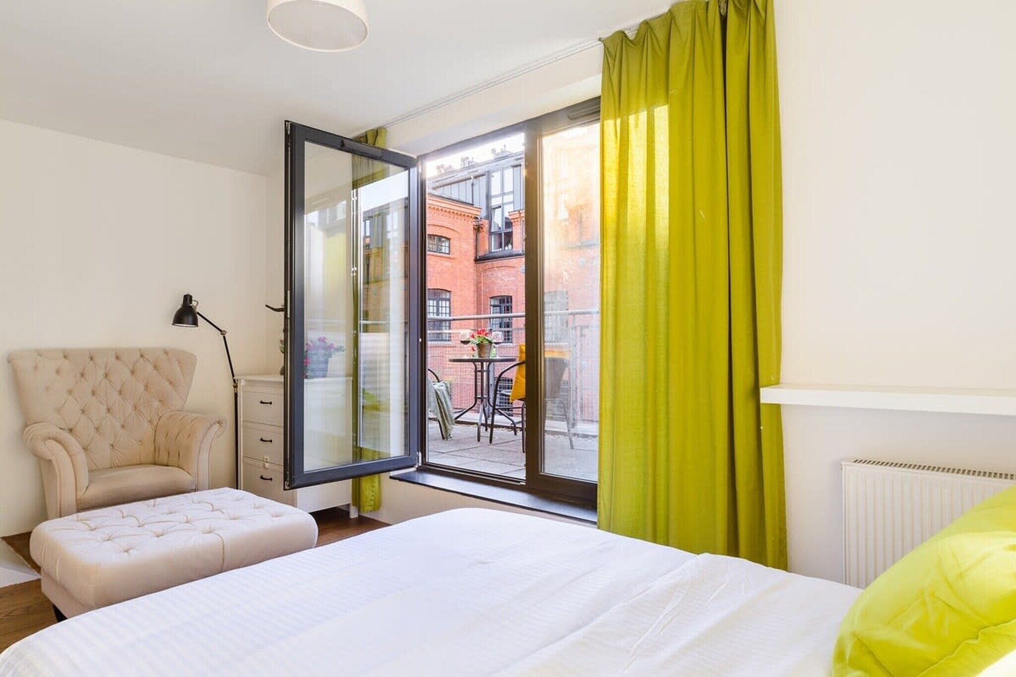 Ein Schlafzimmer mit Bett, Stuhl, Schreibtisch, Lampe und Blick ins Freie.