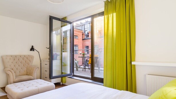 Un dormitorio con cama, una silla, un escritorio, una lámpara y vistas al exterior.
