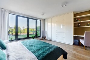 A modern bedroom with a large bed, a seating area, and a balcony with a view. - Loft in Historic Scheibler Area (Łódź)