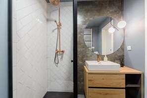 Une salle de bain moderne avec une douche, un lavabo agrémenté d’un miroir rond et un meuble-lavabo en bois.