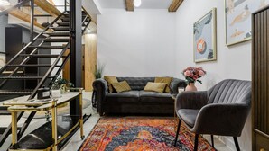 A modern living room with a staircase, a grey sofa, a patterned rug, and a grey armchair. - Duplex Home near Manufaktura (Łódź)