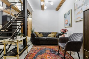 Ein modernes Wohnzimmer mit Treppe, einem grauen Sofa, einem gemusterten Teppich und einem grauen Sessel.