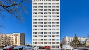 Een meerlaags woongebouw met een gelijkmatig gevelontwerp, meerdere balkons en een parkeerplaats met auto's.