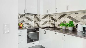 Eine moderne Küche mit weißen Schränken, einem schwarzen Geschirrspüler, einem eingebauten Ofen, einer Edelstahl-Spüle und einer gemusterten Spritzschutzwand.
