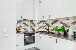 Eine moderne Küche mit weißen Schränken, einem schwarzen Geschirrspüler, einem eingebauten Ofen, einer Edelstahl-Spüle und einer gemusterten Spritzschutzwand.