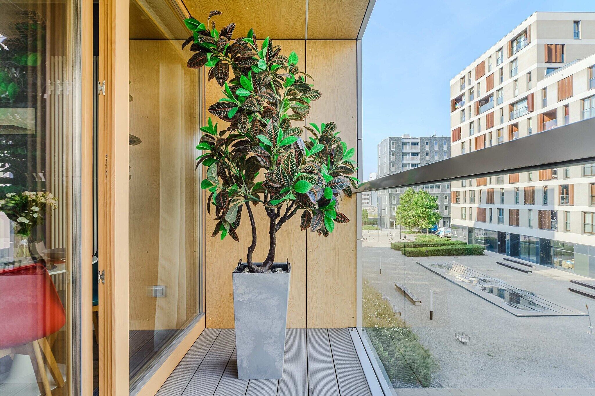 Ein Balkon mit einem Blumentopf, einer Glastür und Blick auf ein modernes Gebäude.