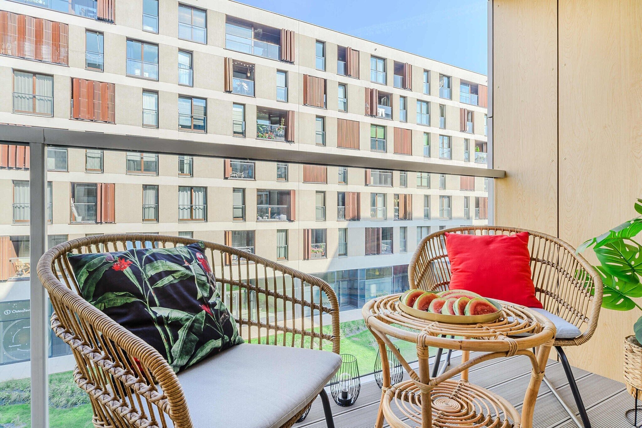A balcony with wicker furniture, a red cushion, and a potted plant.