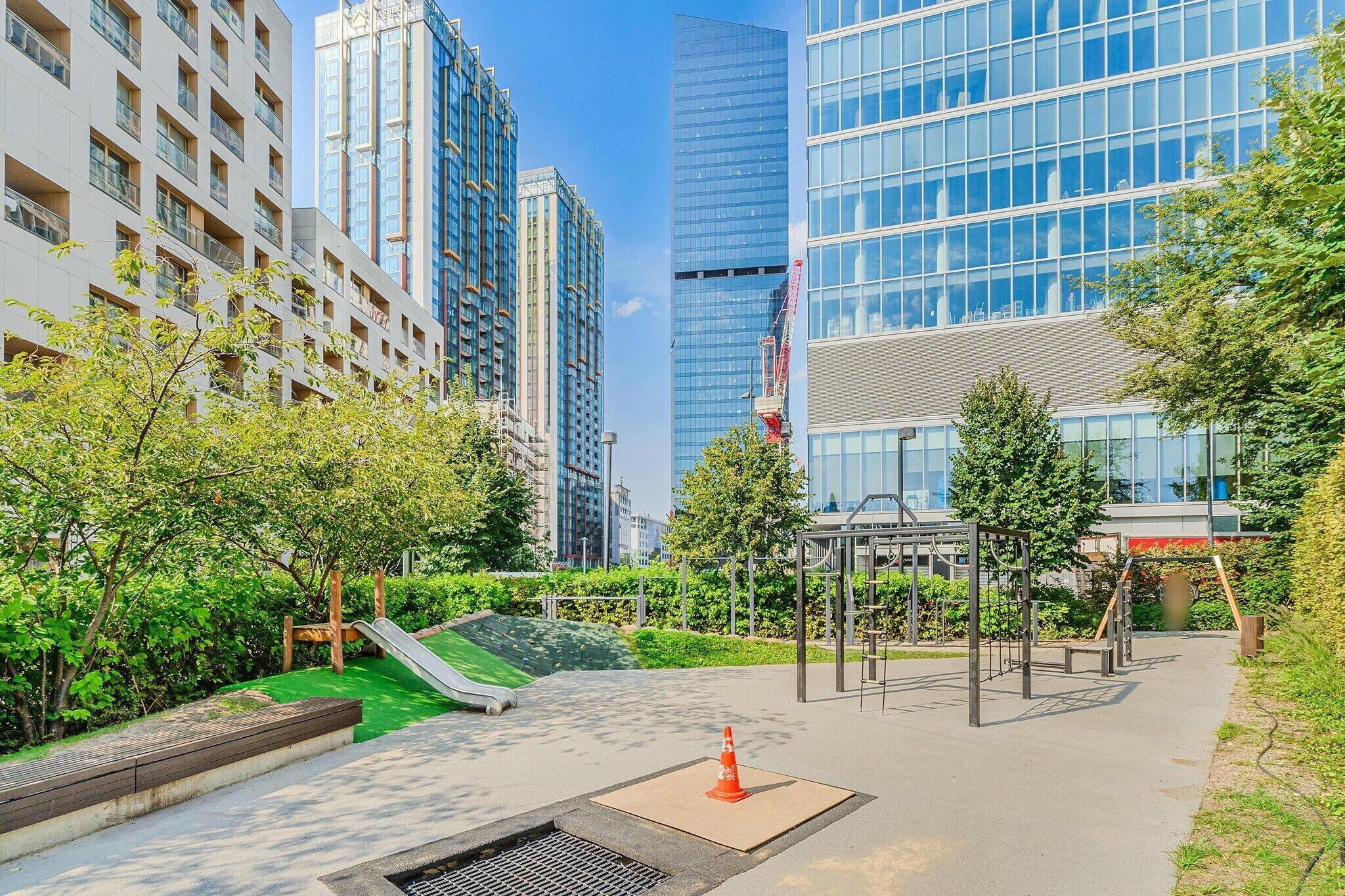 Um parque urbano moderno com equipamentos de playground, um pequeno escorrega e uma área pavimentada.