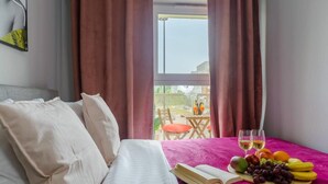Ein Hotelzimmer mit einem Bett, einem Tisch mit Früchten und Getränken sowie Blick ins Freie.