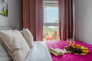 A hotel room with a bed, a table with fruit and drinks, and a view of the outdoors. - Cozy City Retreat for 4 in Warsaw (Łódź)
