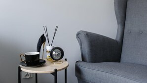 Ein kleiner Tisch mit einer schwarzen Tasse, einer Uhr und einer Flasche Eryfe. Ein grauer Sessel befindet sich rechts davon.
