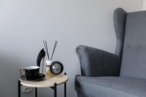 A small table with a black cup, a clock, and a bottle of Eryfe. A grey armchair is positioned to the right. - Cozy City Retreat for 4 in Warsaw (Łódź)