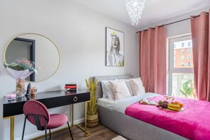 A modern bedroom with a bed, a desk, a chair, a mirror, a window with curtains, and a chandelier. - 3-Bedroom Łódź Apartment with Balcony (Łódź)