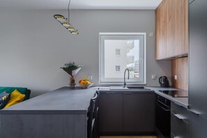 A modern kitchen with a central island, a built-in oven, and a window overlooking a residential area. - 3-Bedroom Łódź Apartment with Balcony (Łódź)