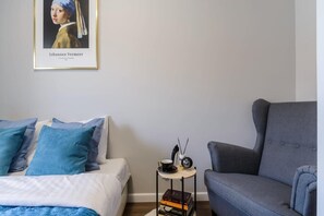 A bedroom with a bed, a grey armchair, a small table with a cup and books, and a framed picture on the wall. - Cozy City Retreat for 4 in Warsaw (Łódź)