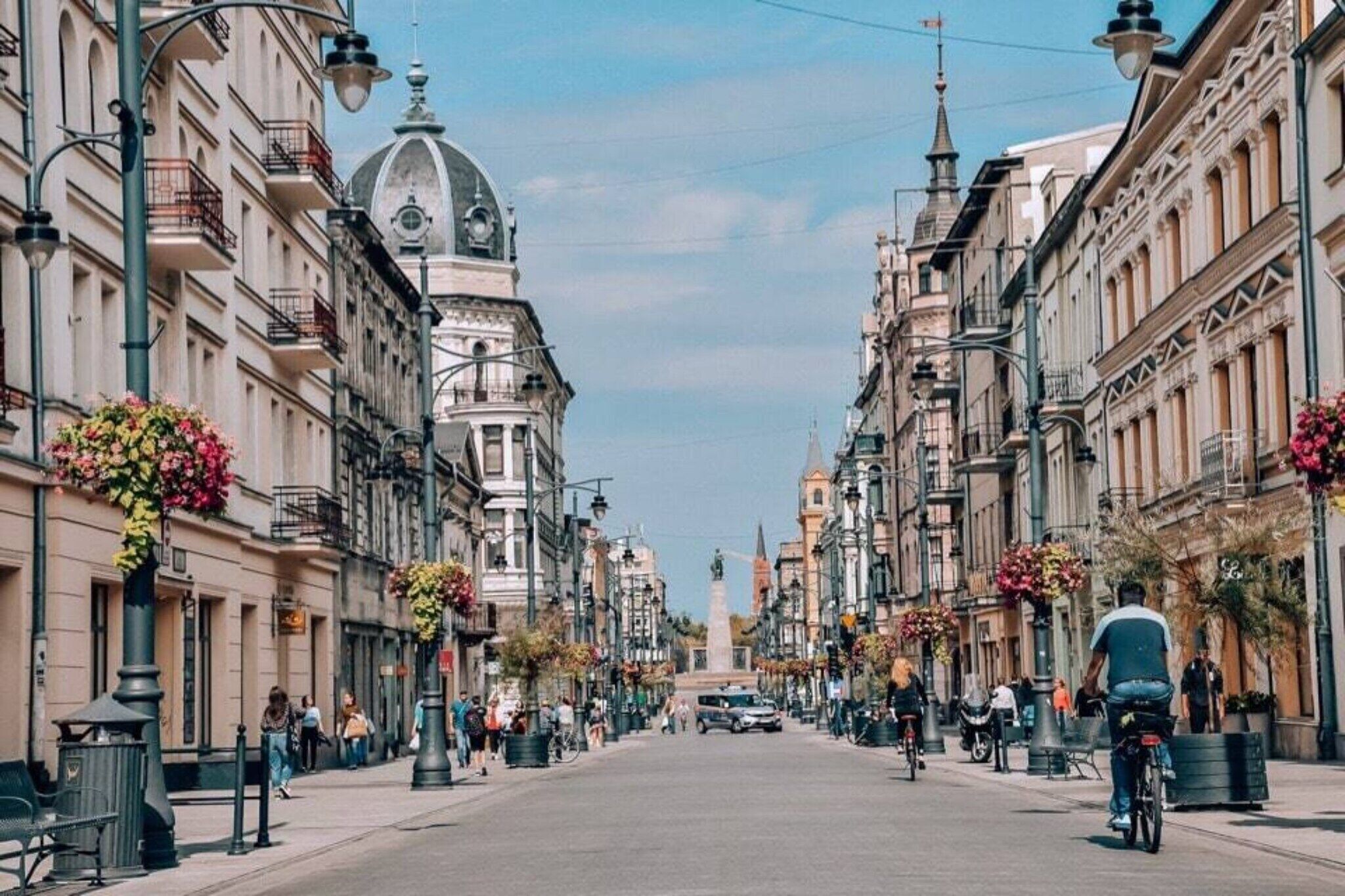 A street lined with historic buildings, a central monument, and flower arrangements on the sidewalks.