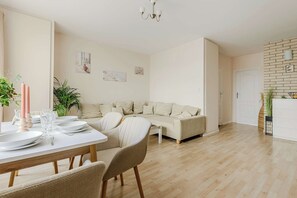 Ein modernes Wohnzimmer mit einer Couch, einem Esstisch mit Tellern und Gläsern, einer Chandelierleuchtre und einer Ziegelwand.