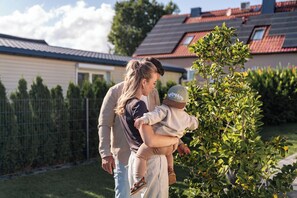 Eine Familie in einer Wohngegend mit Haus, umzäuntem Garten und Baum.