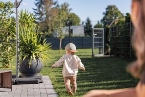 A child walking on a paved path in a garden area with a large potted plant and a metal fence in the background. - Landliebe Lodges "Bienenstock" Vacation Home - Country Life, Dinopark, Hollandpark, Thermal Baths (Löwenberger Land)
