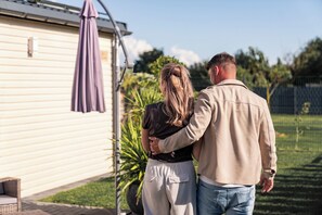 A couple standing in front of a mobile home with a patio umbrella. - Landliebe Lodges "Bienenstock" Vacation Home - Country Life, Dinopark, Hollandpark, Thermal Baths (Löwenberger Land)