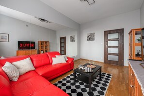 A modern living room with a red sectional sofa, a black and white patterned rug, a coffee table with decorative items, a wooden cabinet, and a television displaying the word 'NETFLIX'. - City View Apartment in Warsaw (Warszawa 2)