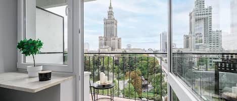 Un balcón con vista a edificios de la ciudad, una planta en maceta y una pequeña mesa con velas.