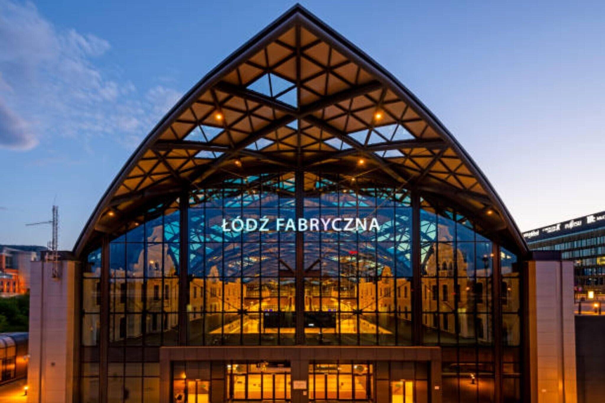 A modern building with a glass facade and a prominent sign reading 'LÓDZ FABRYCZNA'.