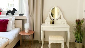 Hotellihuone, jossa on sänky, yöpöytä lampun kanssa, peilillä varustettu meikkipöytä ja pieni jakkara.