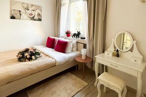 A bedroom with a bed, a bedside table, a dresser, a mirror, and a window with curtains. - Lodz Apartment for 4 Guests (Łódź)
