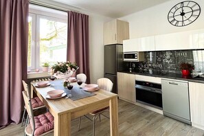 A modern kitchen with a dining area, featuring a wooden table, chairs, a clock, and a refrigerator. - Lodz Apartment for 4 Guests (Łódź)