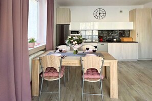 A modern kitchen with a dining table set for four, a clock on the wall, and a chalkboard with coffee-related drawings. - Lodz Apartment for 4 Guests (Łódź)