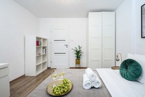 A modern bedroom with a bed, a bedside table, a nightstand, a wardrobe, a bookshelf, and a small potted plant. - Lush Stay on Przasnyska (Warszawa 2)