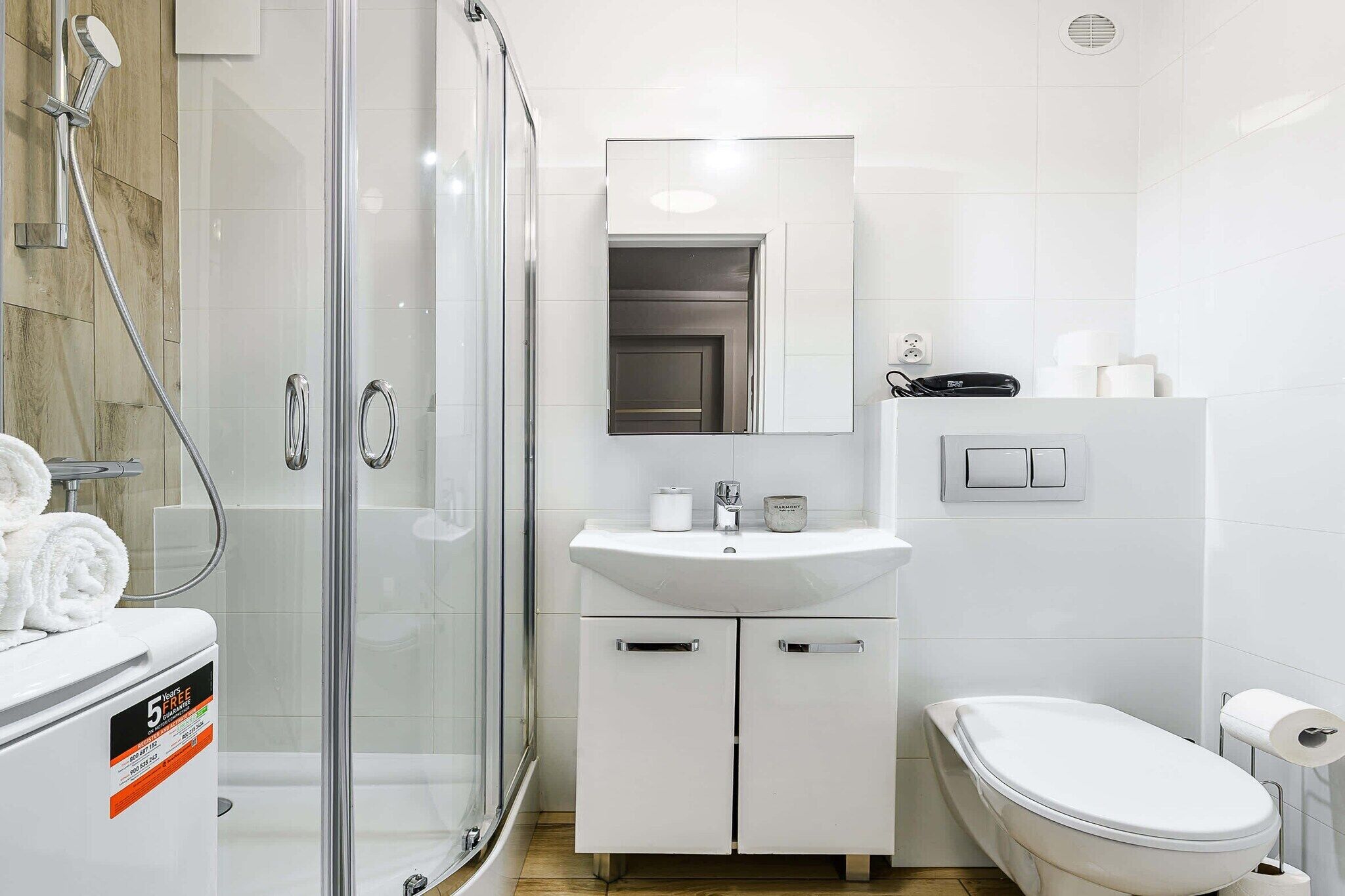 Un baño moderno con cabina de ducha de vidrio, un lavamanos blanco, un inodoro y un espejo sobre el lavamanos.