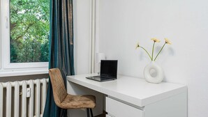 A modern office space with a white desk, a laptop, a chair, a vase with flowers, and a window with curtains. - Lush Stay on Przasnyska (Warszawa 2)